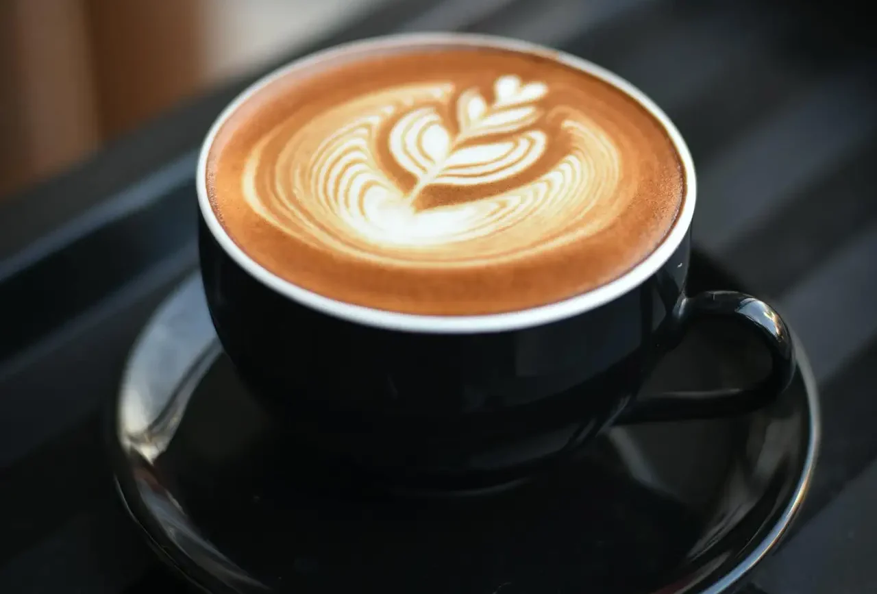 A beautifully crafted cappuccino with intricate latte art in a black ceramic mug on a dark surface.